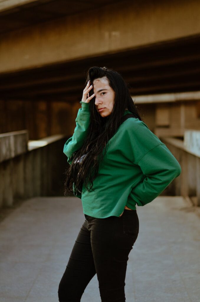 side view photo of beautiful woman with vitiligo in green sweatshirt and black pants posing in middle of concrete pathway