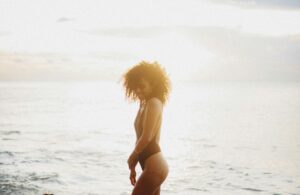 slim ethnic woman in bikini standing in water